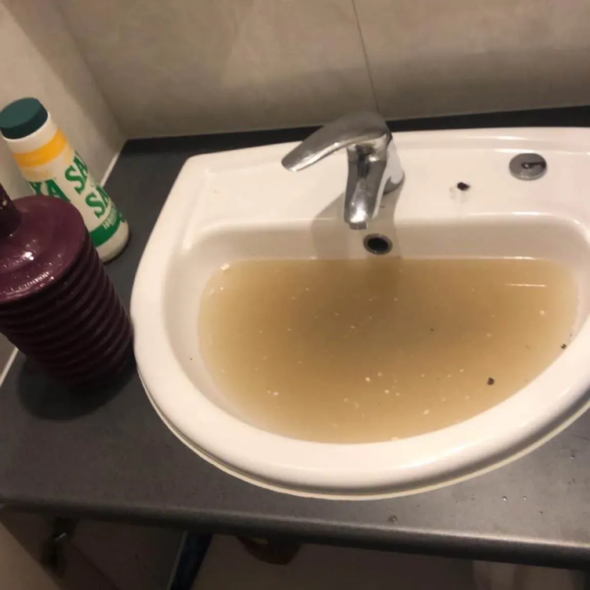 Blocked bathroom basin holding dirty water