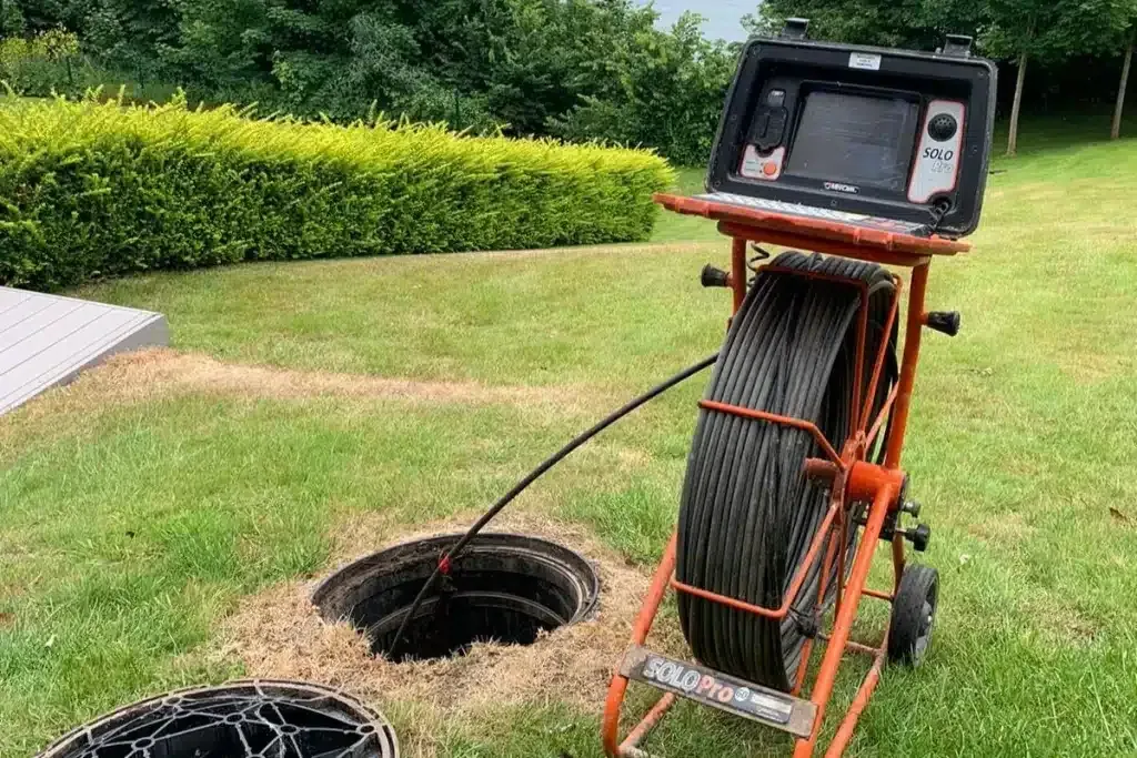 Drain inspection camera reel lowered into a pit in a lawn