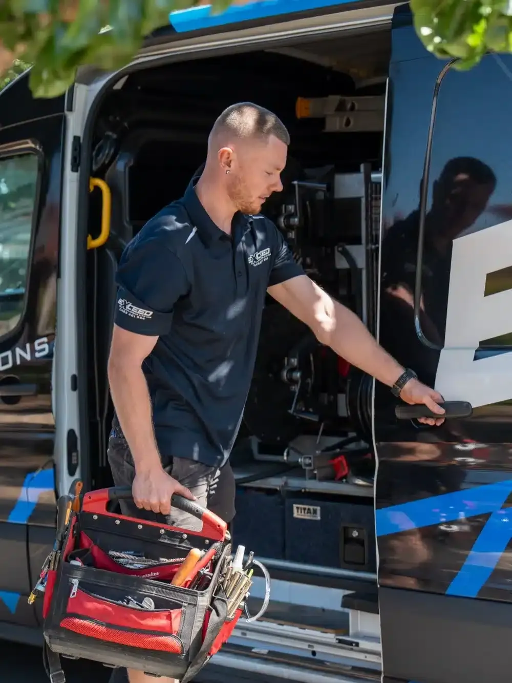 Caleb John of Exceed Plumbing taking his tool bag from the side door of the service van
