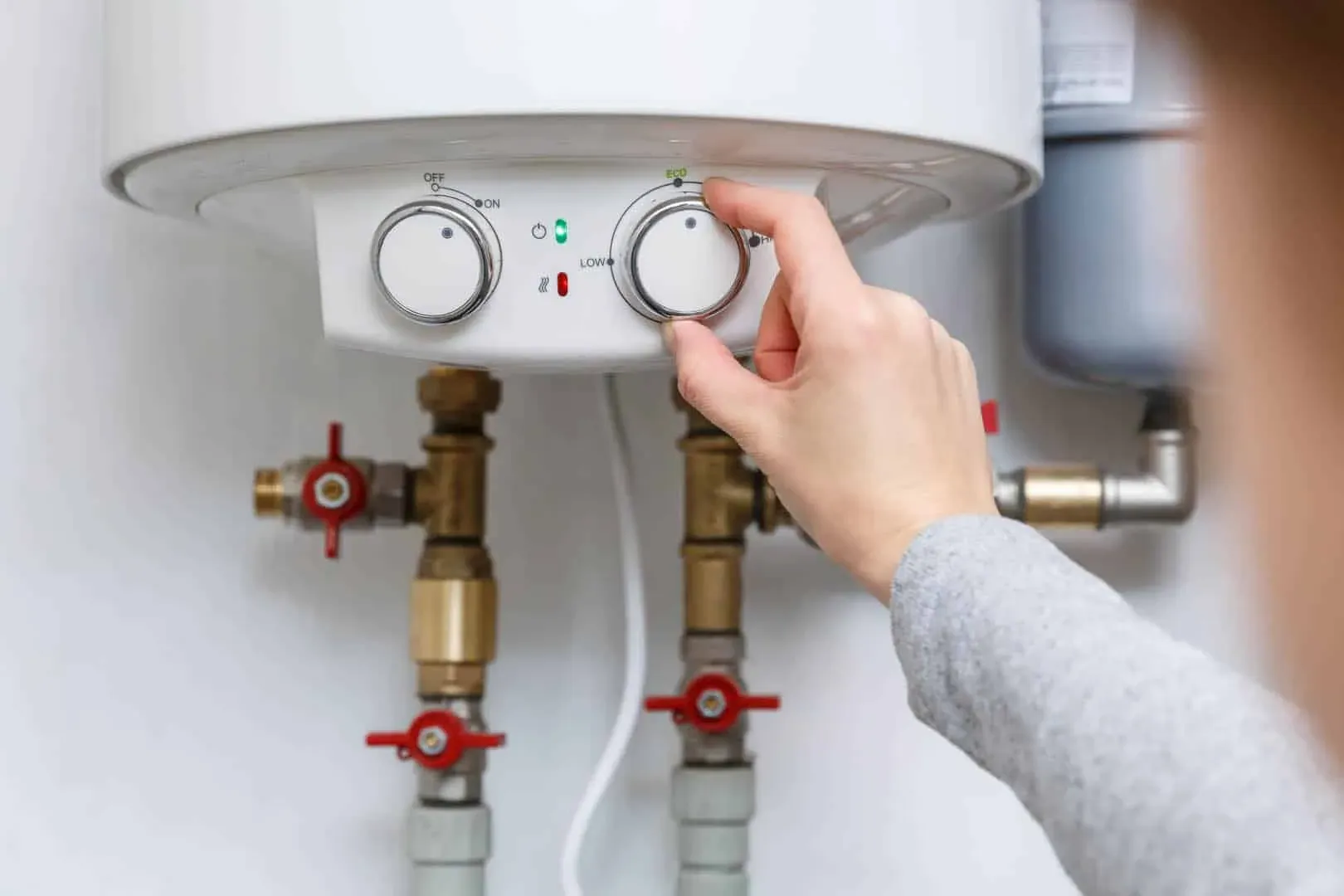 Hand adjusting the thermostat dial on an electric hot water unit
