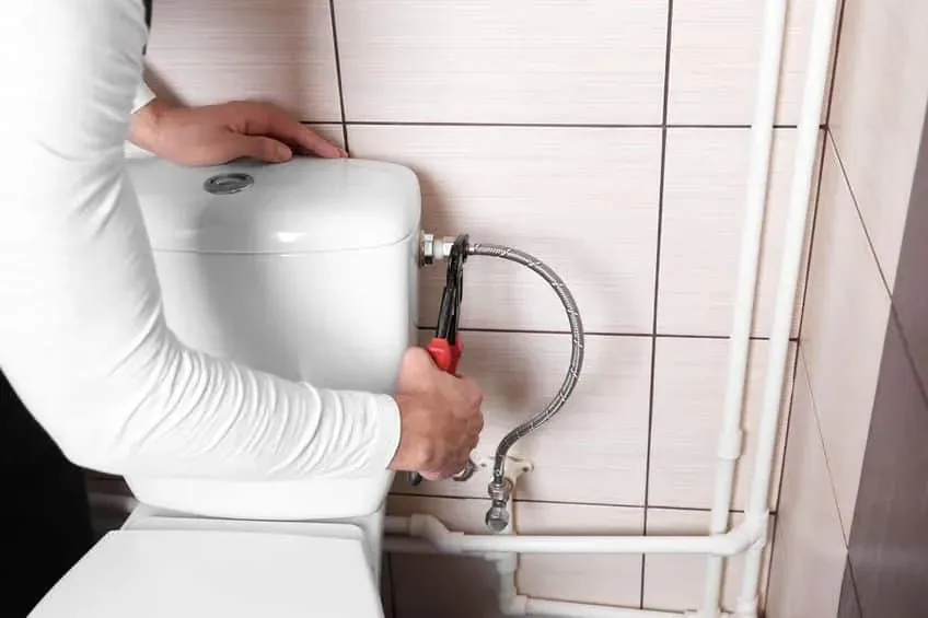 Hands tightening the water connection to a toilet cistern