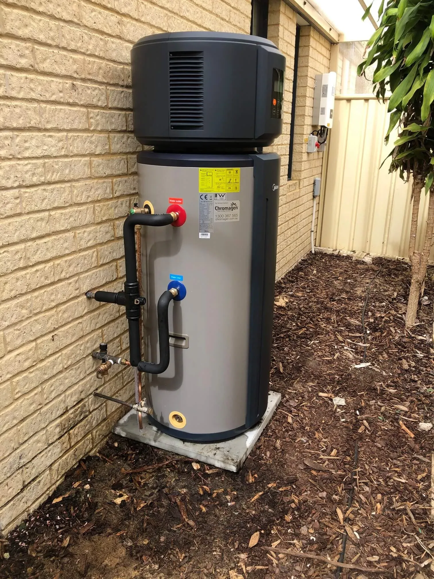 Newly installed heat pump hot water system beside a brick wall