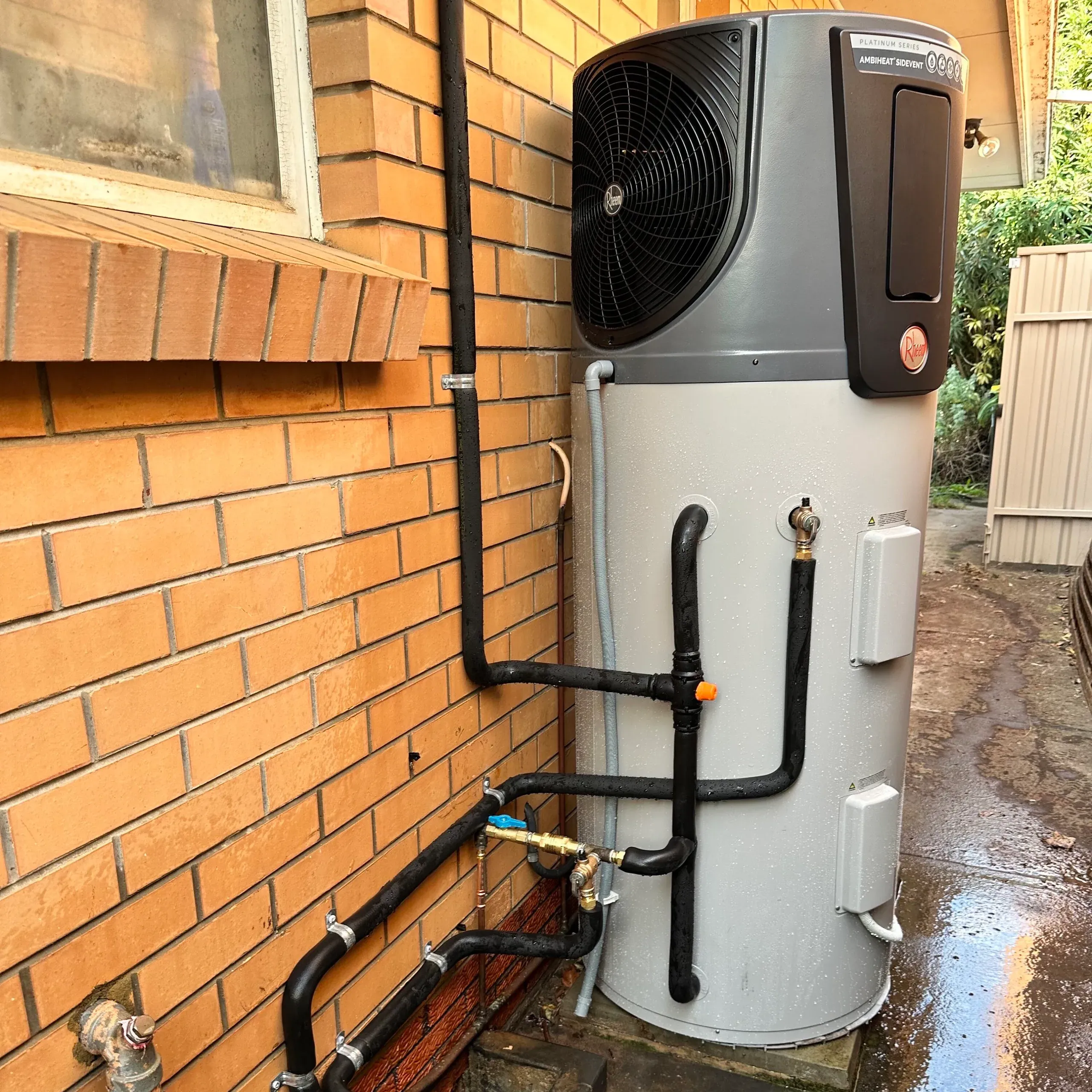 Heat pump hot water system installed against a brick wall
