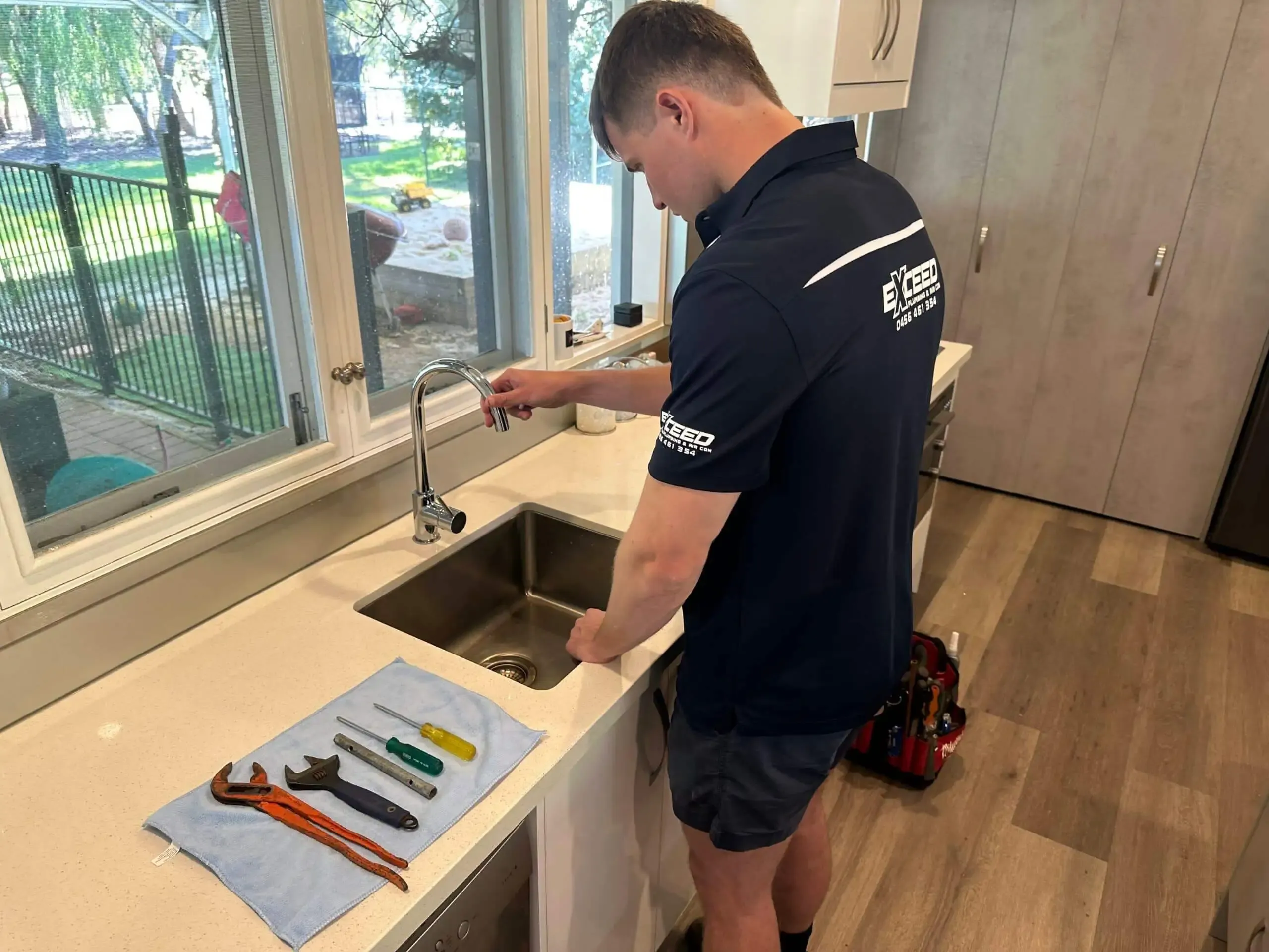 Exceed Plumbing plumber at a kitchen sink, his tools still laid out on the bench
