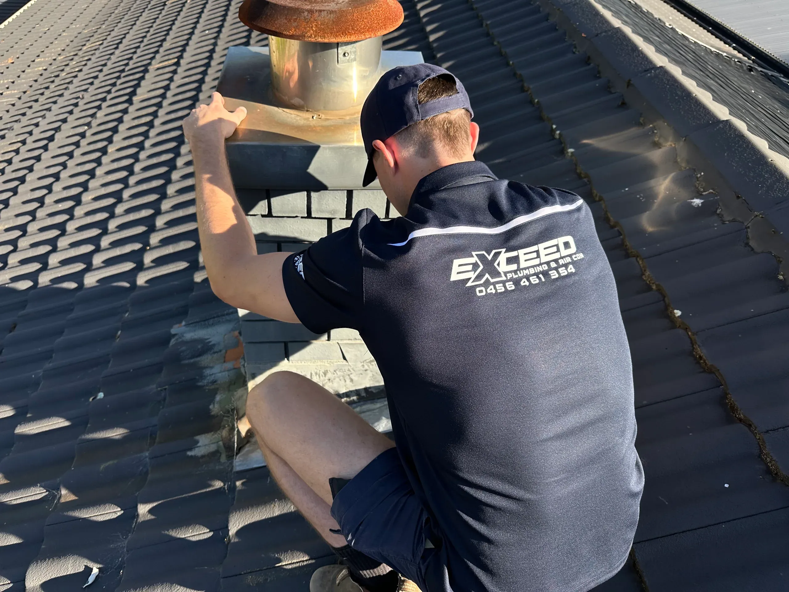 Exceed Plumbing plumber checking the flashing around a flue on a tiled roof