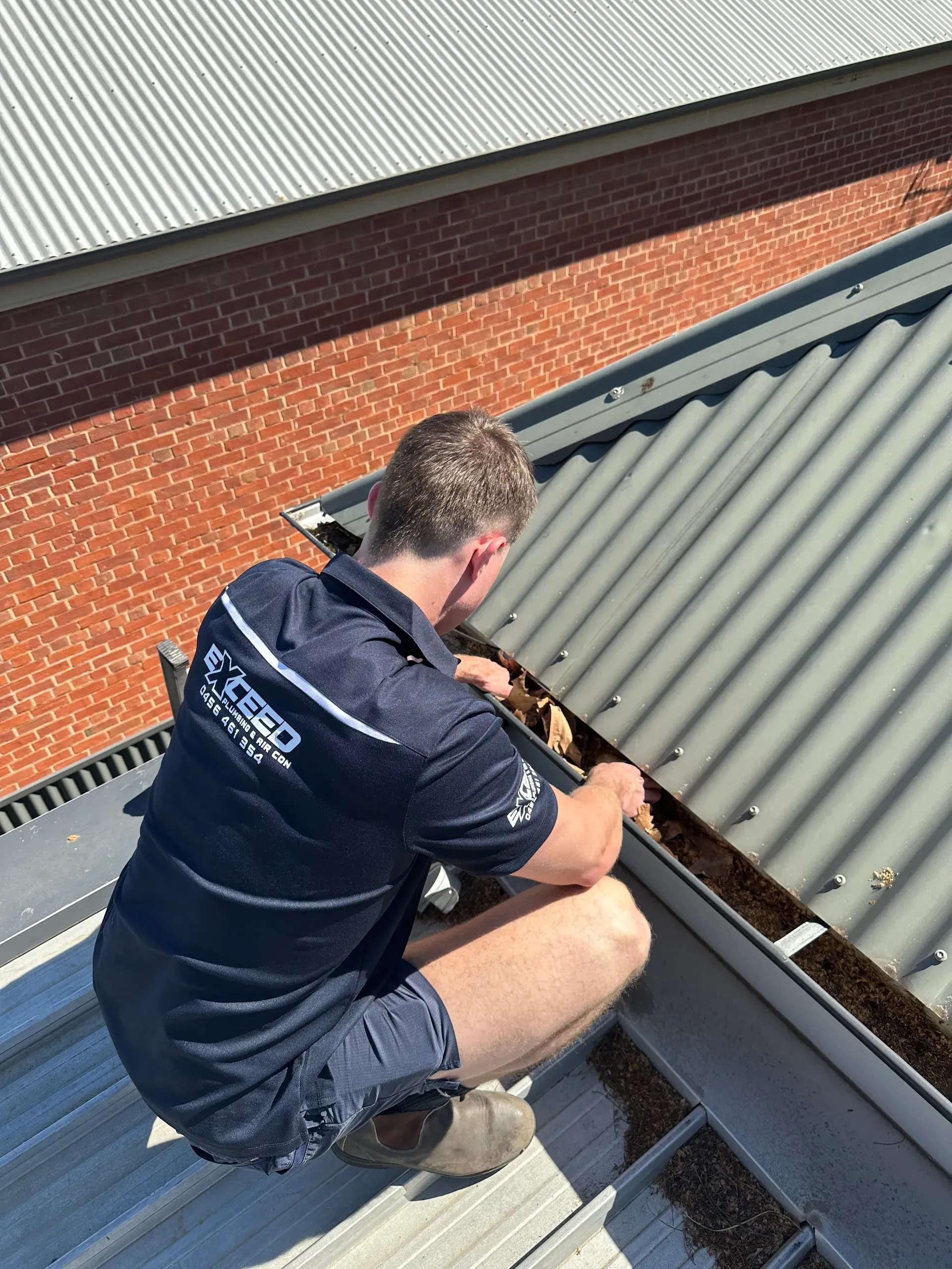 Exceed Plumbing plumber clearing a box gutter on a metal roof