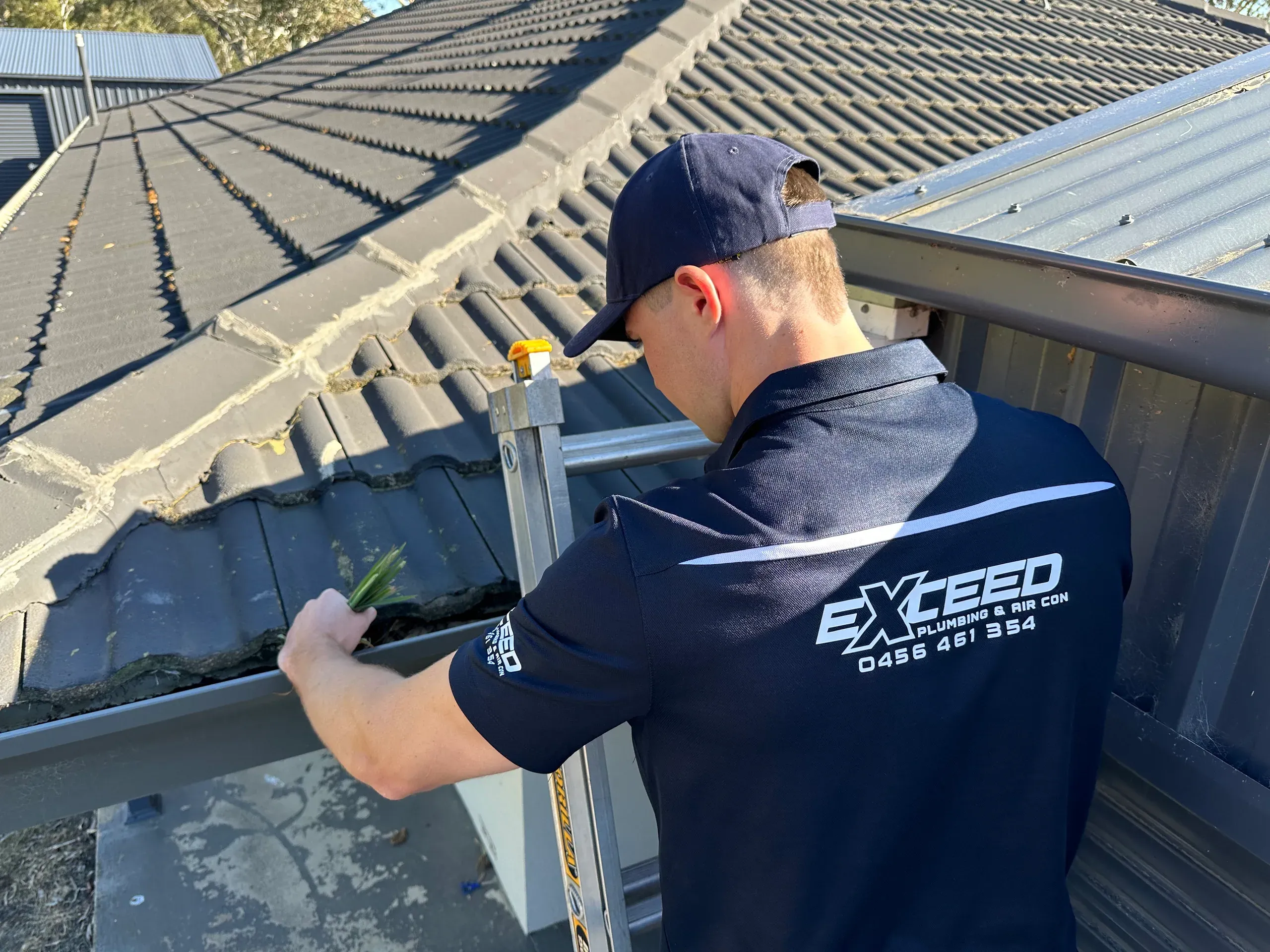 Exceed Plumbing plumber clearing debris from a roof gutter