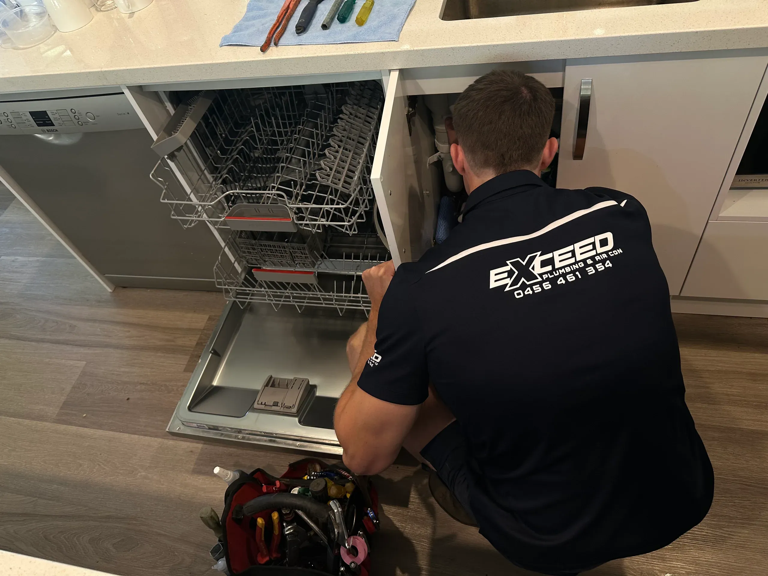 Exceed Plumbing plumber connecting a dishwasher under a kitchen bench