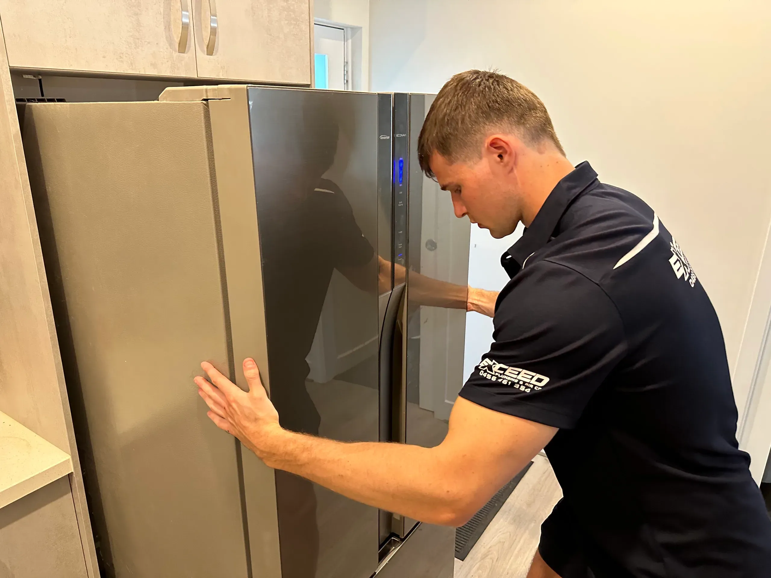 Exceed Plumbing plumber easing a plumbed fridge back into its cavity