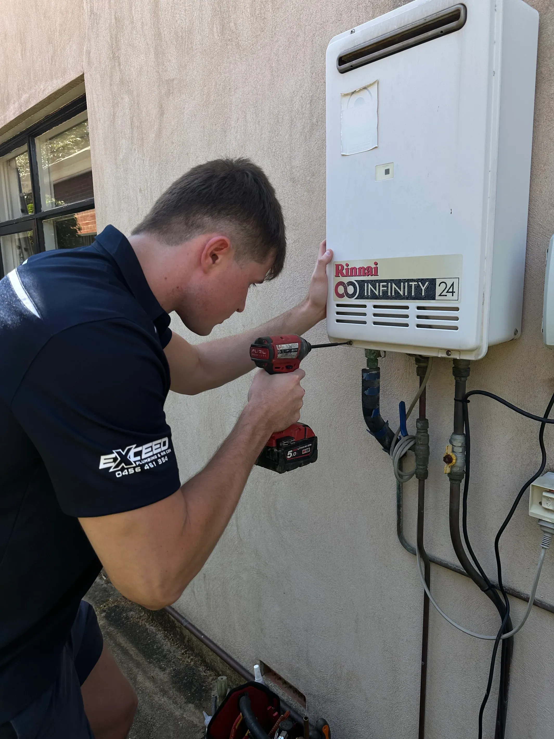 Exceed Plumbing plumber in uniform working on a Rinnai continuous flow hot water unit