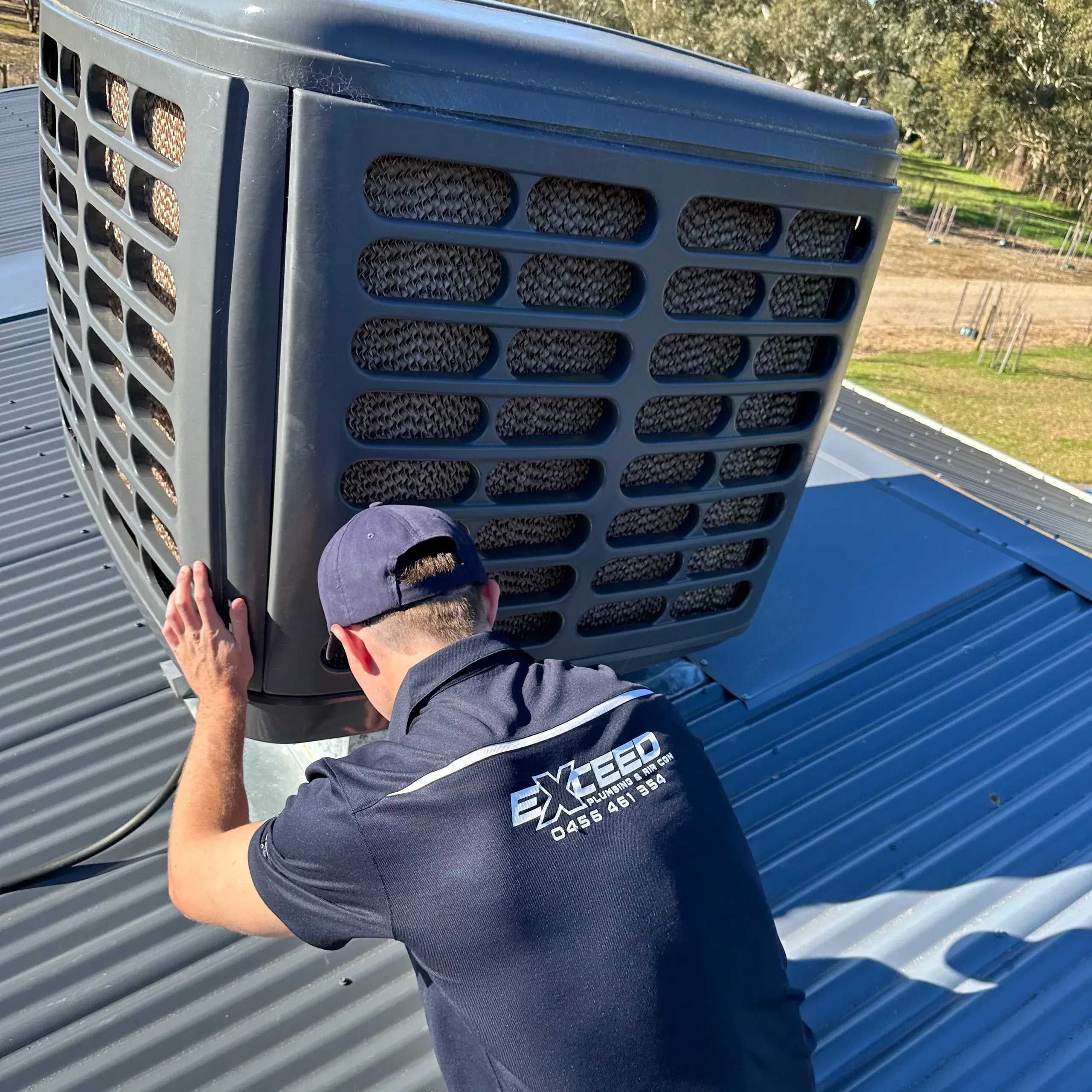 Exceed Plumbing technician servicing a rooftop evaporative cooler