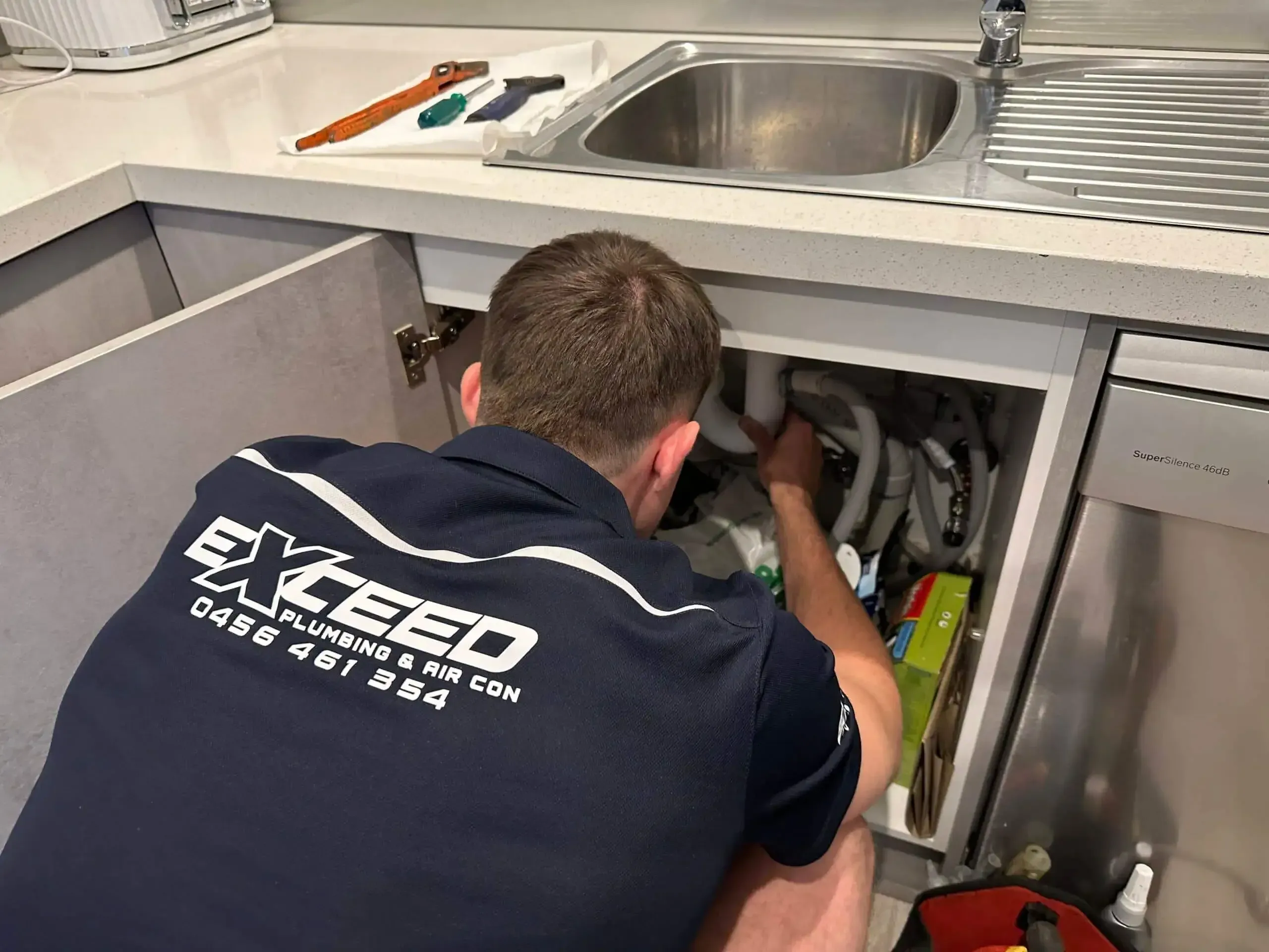 Exceed Plumbing plumber working on the pipes under a kitchen sink