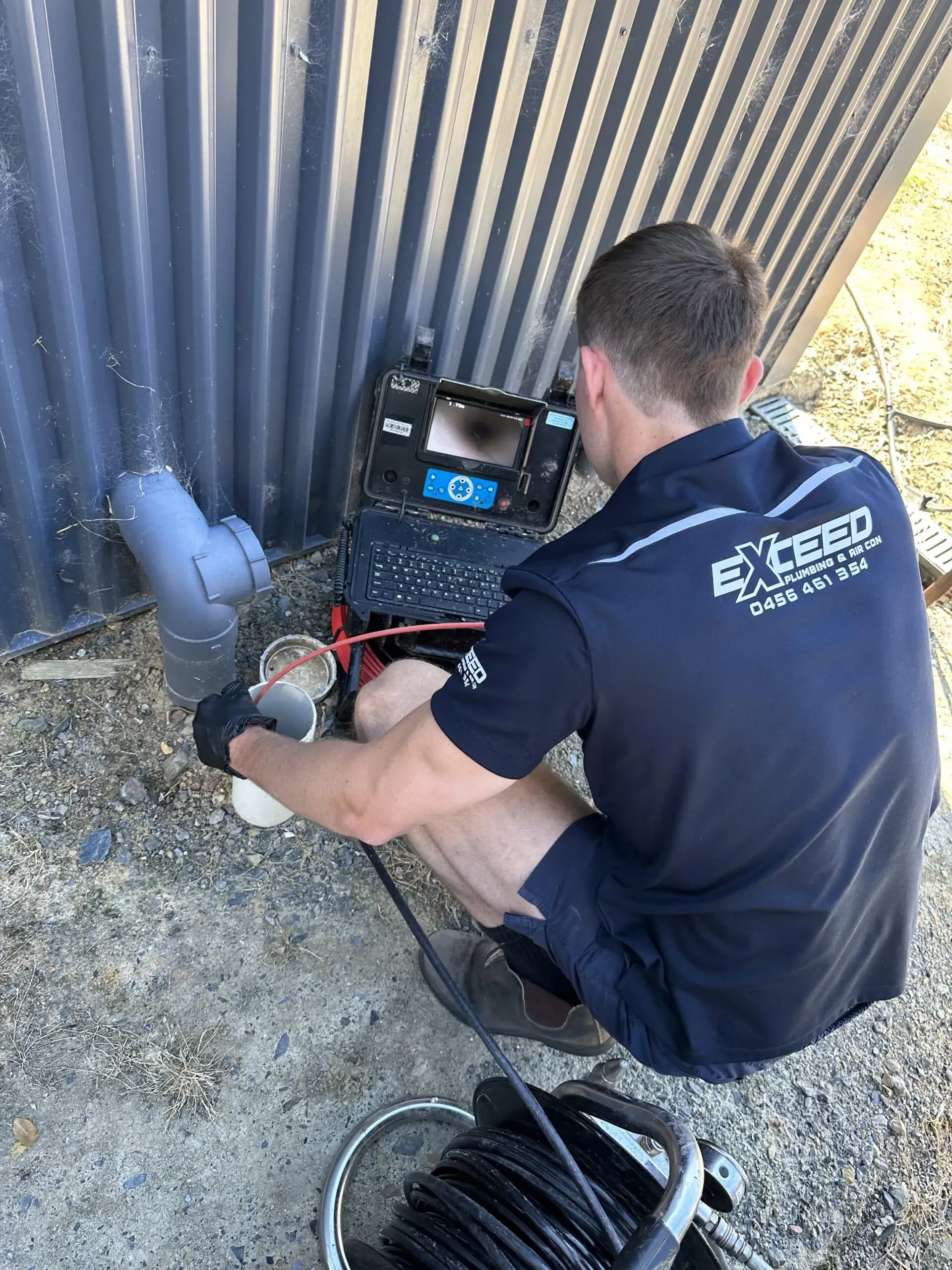 Exceed Plumbing plumber running a CCTV camera into a sewer drain, the monitor beside him