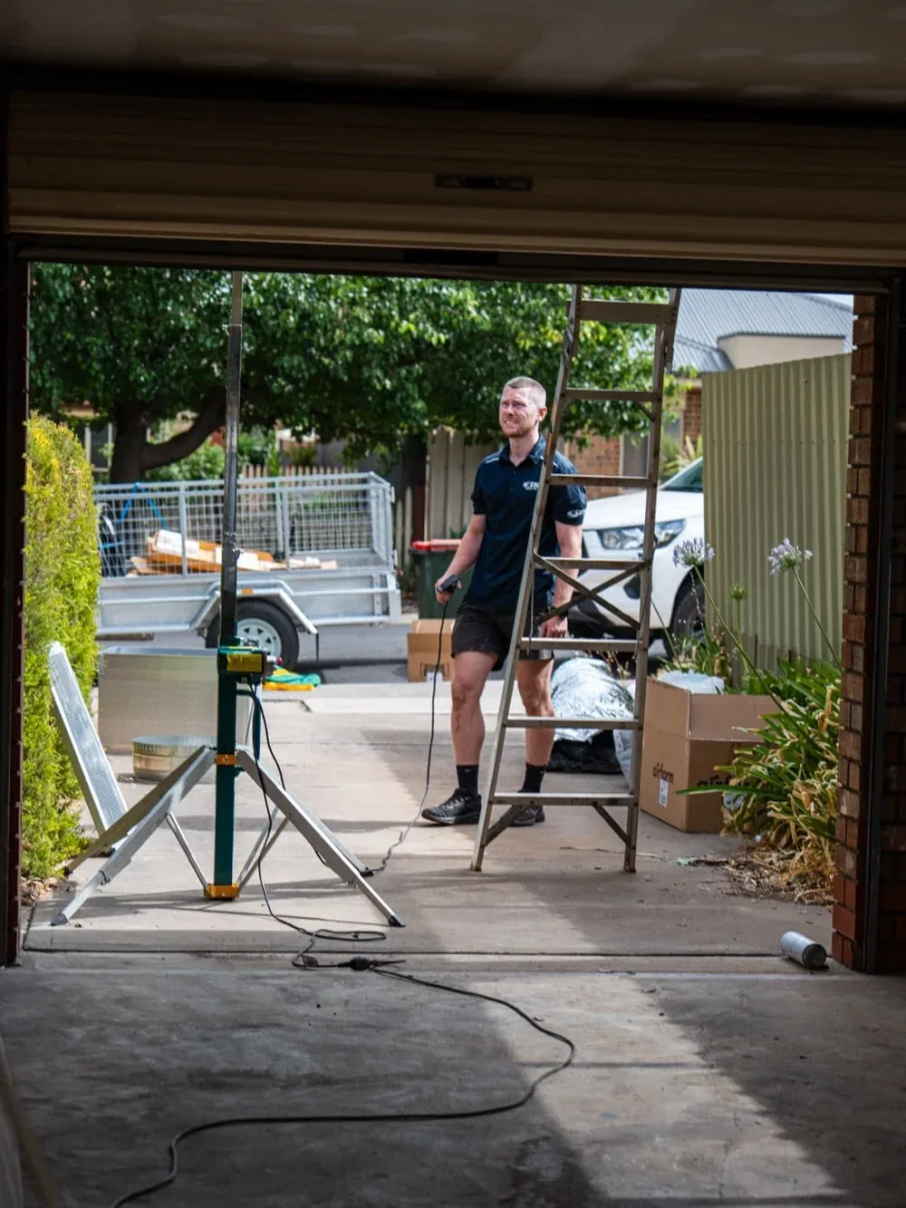 Exceed Plumbing technician on a ladder in a garage during a ducted air conditioning install