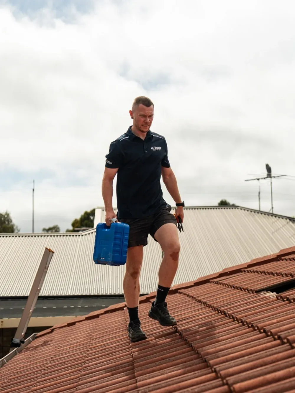 Exceed Plumbing technician walking across a tiled roof with a toolbox