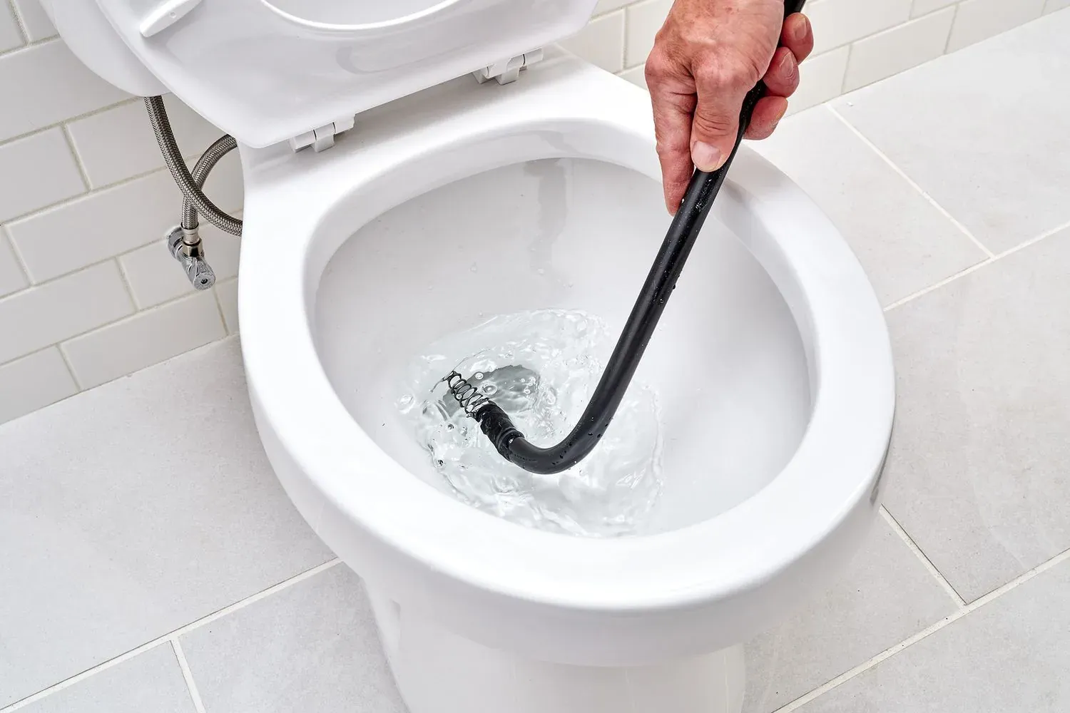 Toilet auger being fed into a blocked toilet bowl