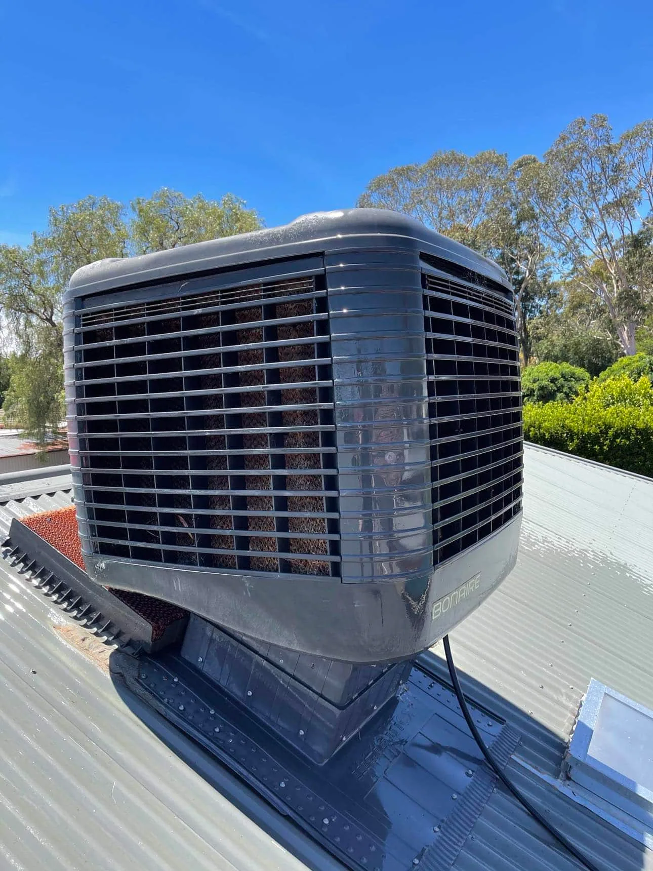 Evaporative cooler on a metal roof against a blue sky