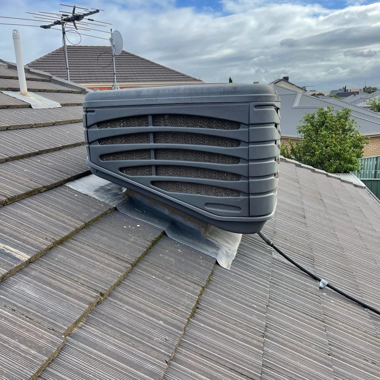 Grey evaporative cooler on a tiled roof