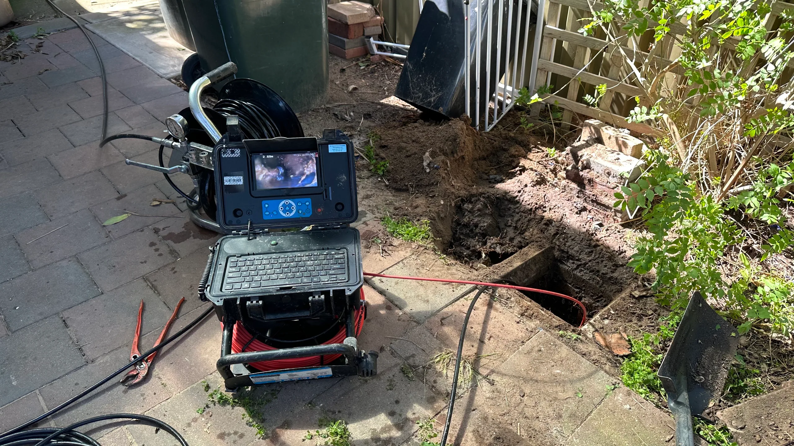 Drain inspection camera beside an excavated drain in a garden