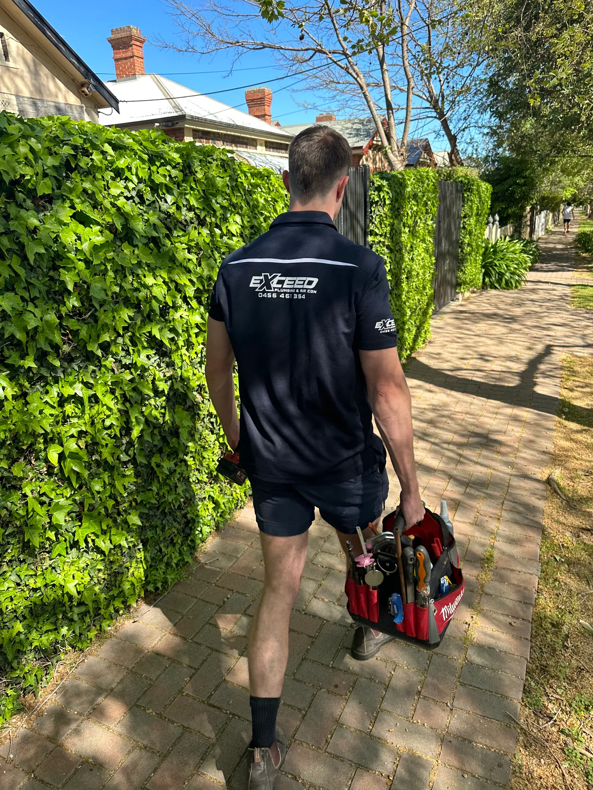 Exceed Plumbing plumber walking along a footpath with a toolbag