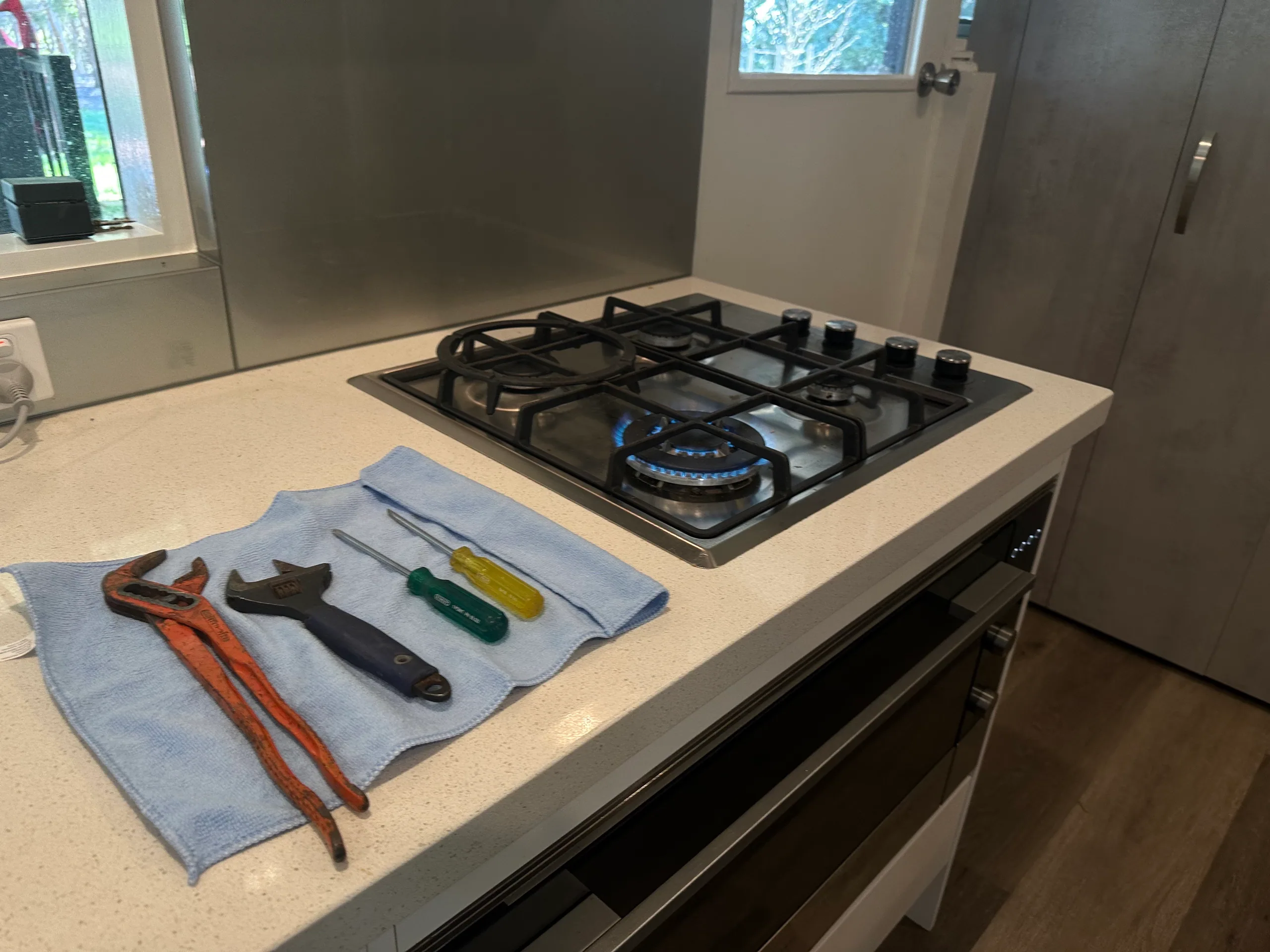 Gas cooktop with a burner lit and tools laid out on the bench