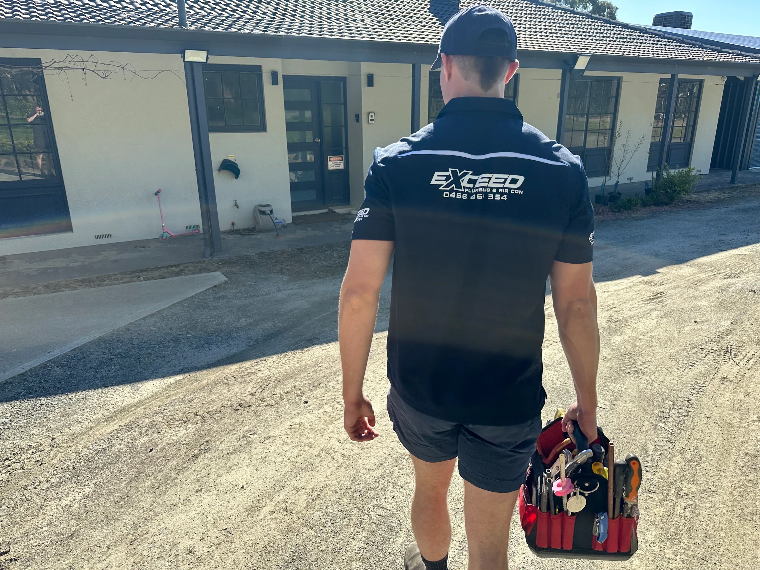 Exceed Plumbing plumber walking to a house with his toolbag