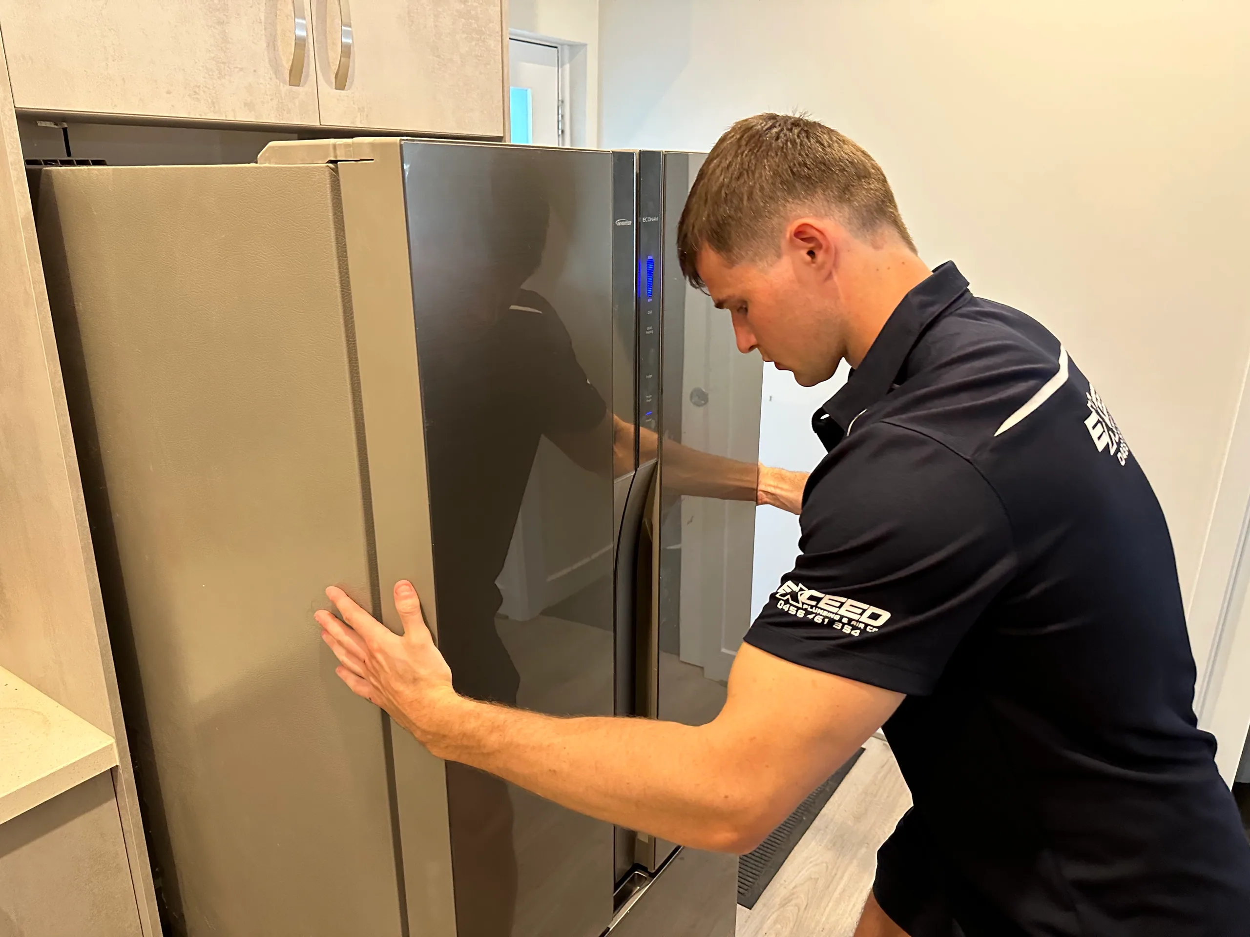 Exceed Plumbing plumber positioning a fridge in a kitchen