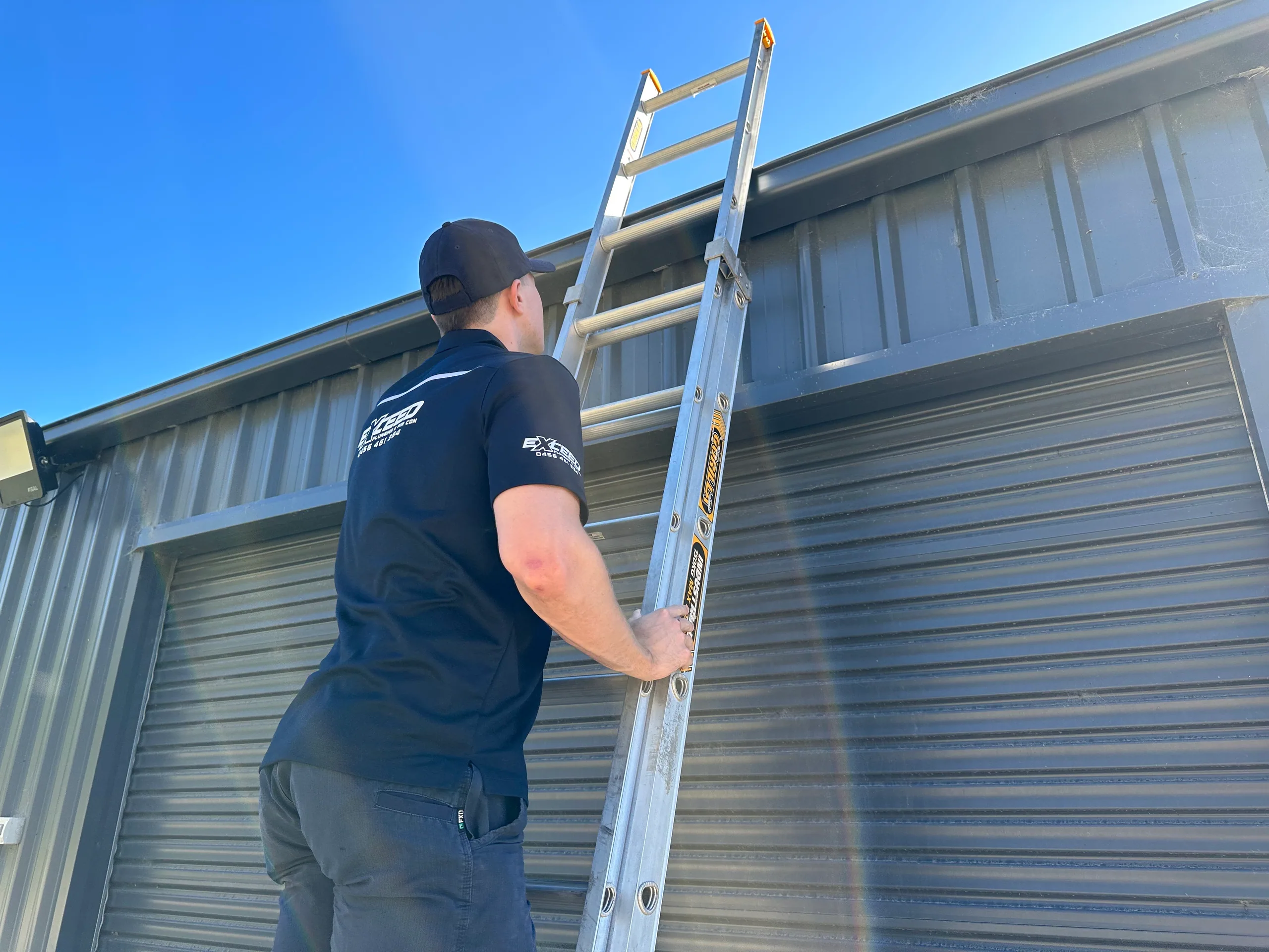 Exceed Plumbing plumber climbing a ladder against a shed