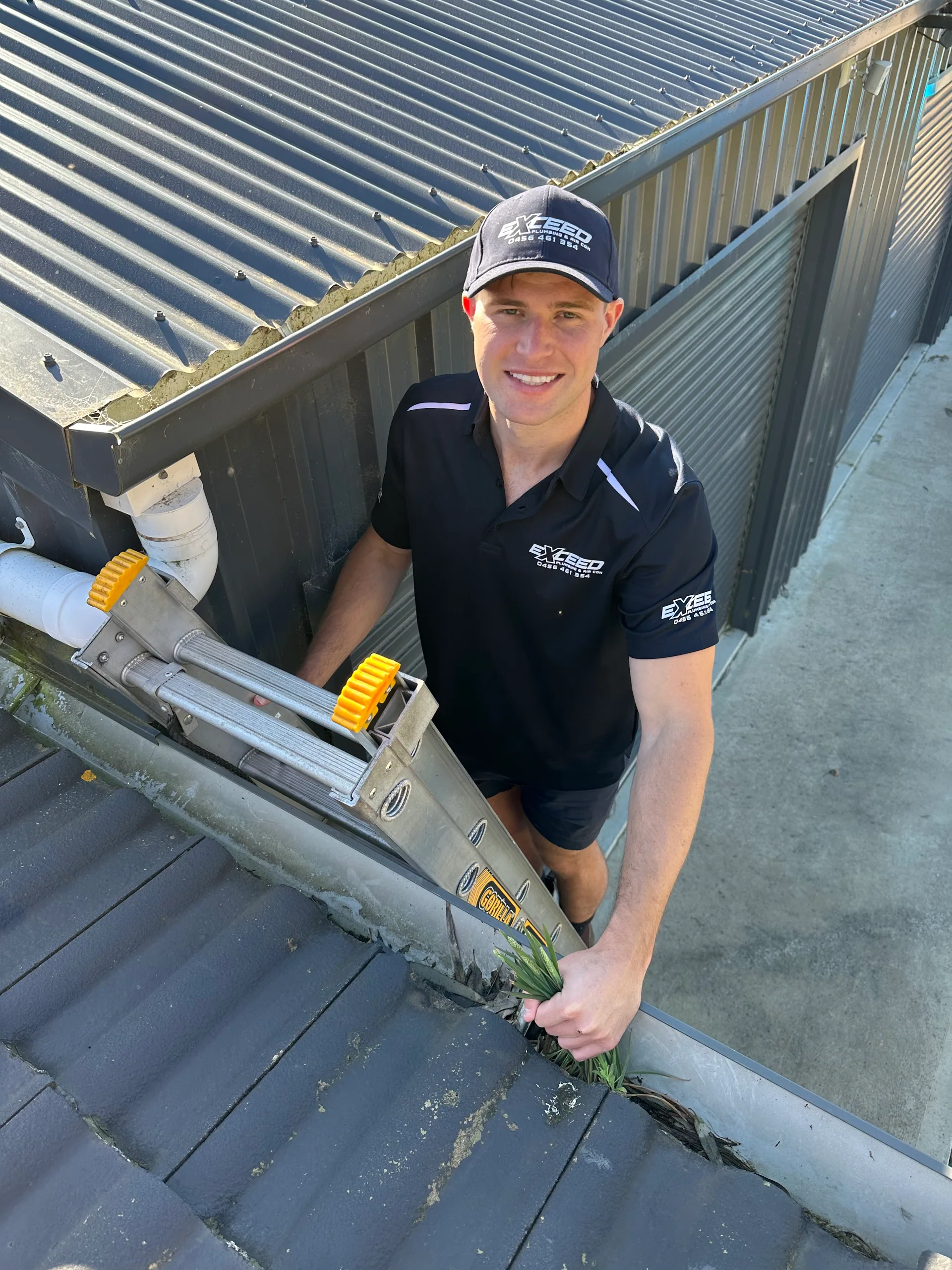 Exceed Plumbing plumber on a ladder clearing a gutter