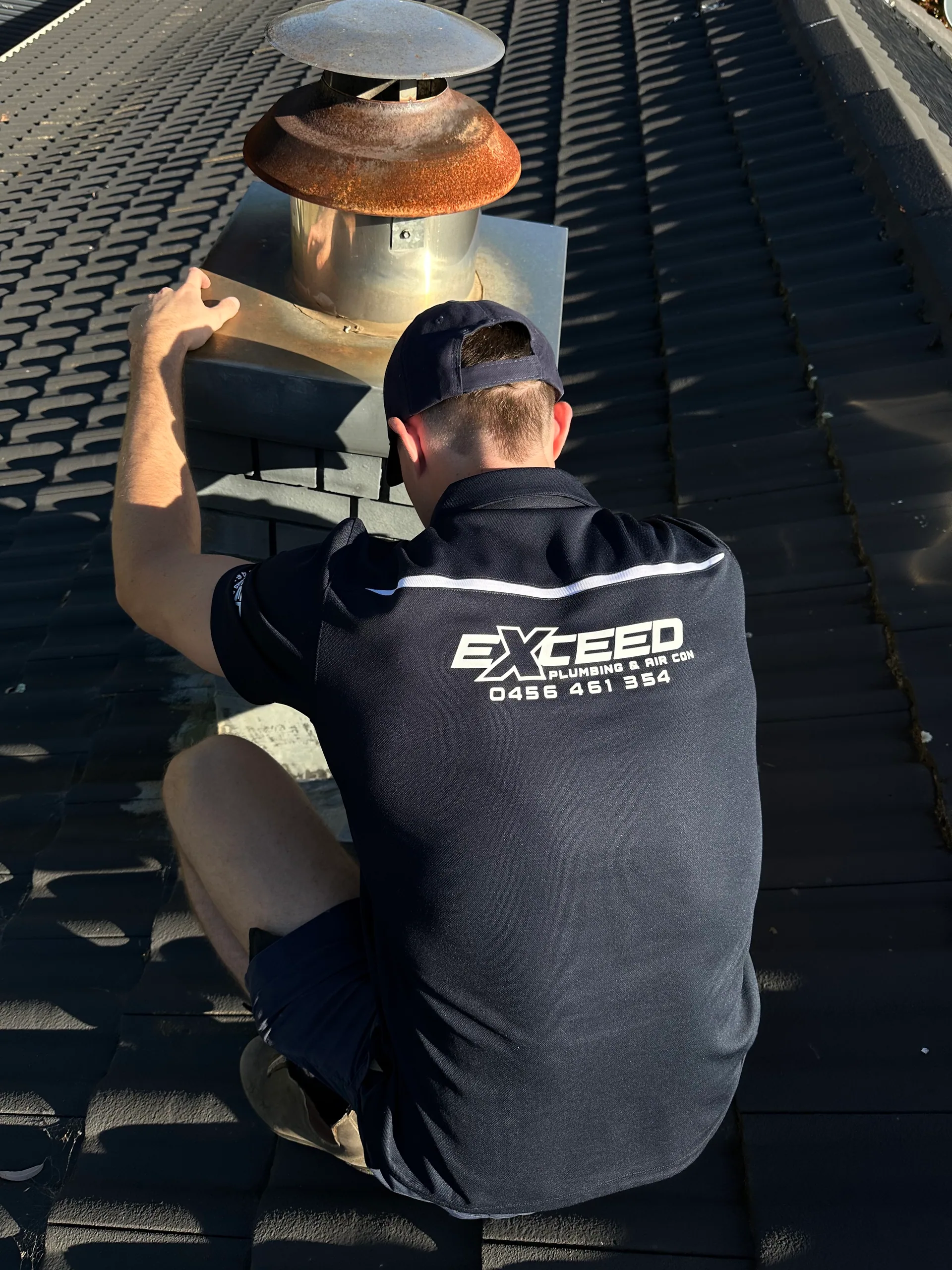 Exceed Plumbing plumber checking a flue cowl on a tiled roof