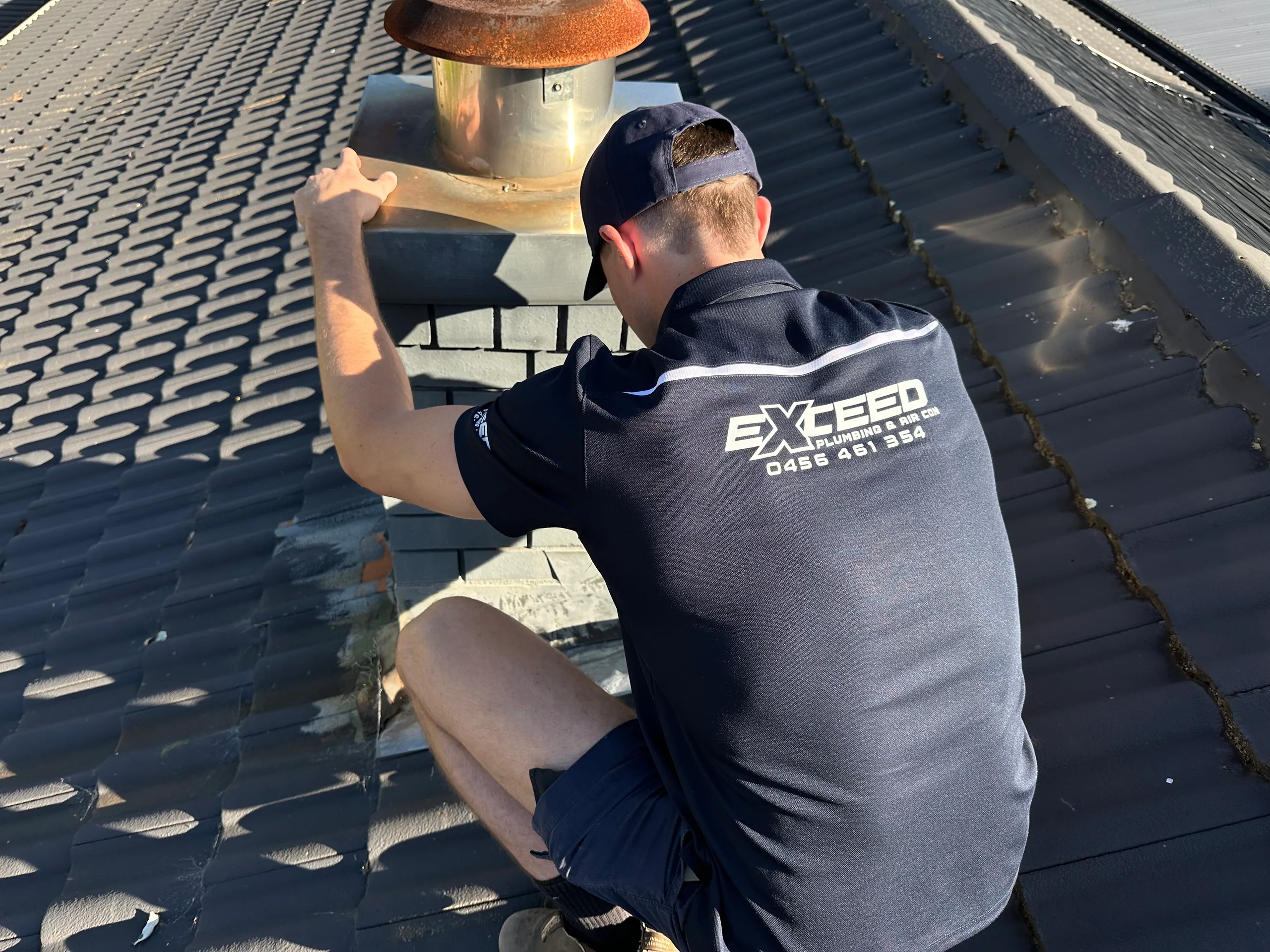 Exceed Plumbing plumber working on a flue on a tiled roof