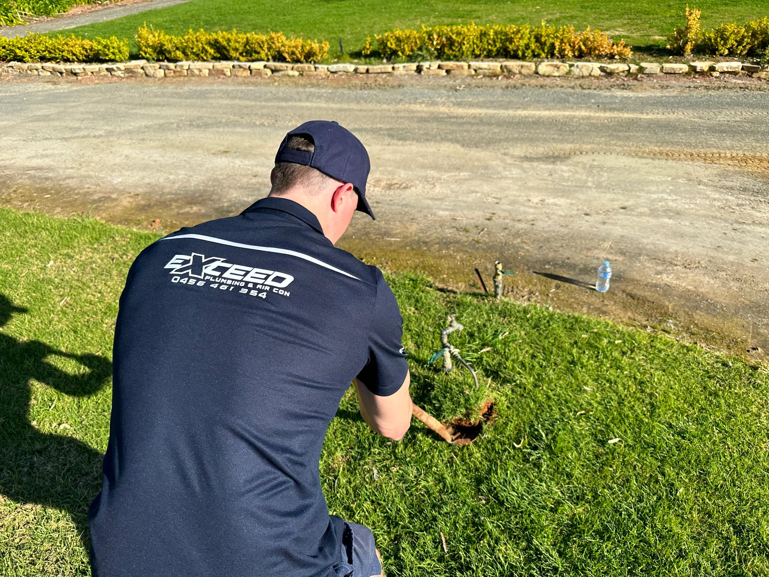 Exceed Plumbing plumber digging beside a garden tap on a lawn