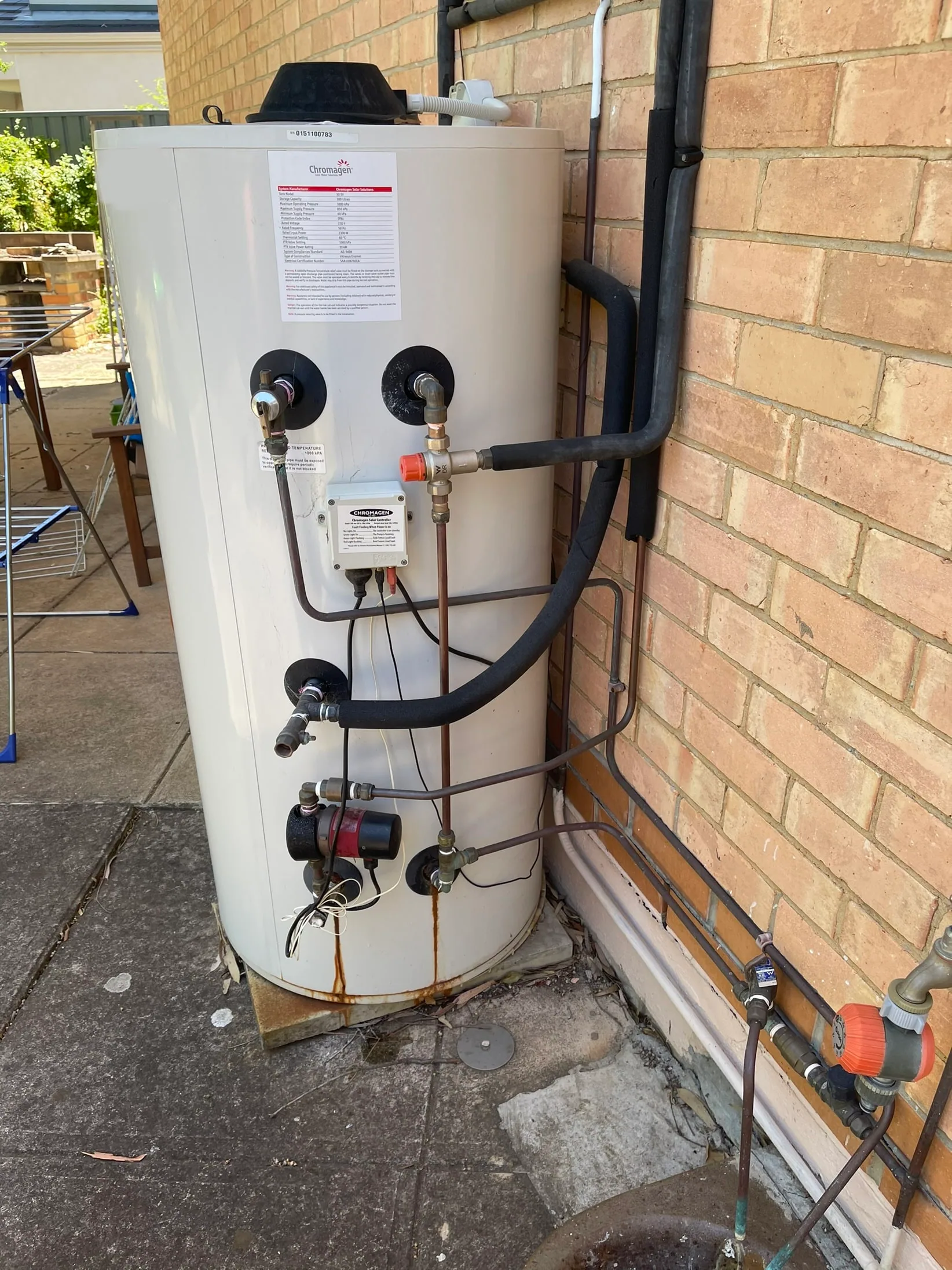 Hot water storage tank with a pump and pipework against a brick wall