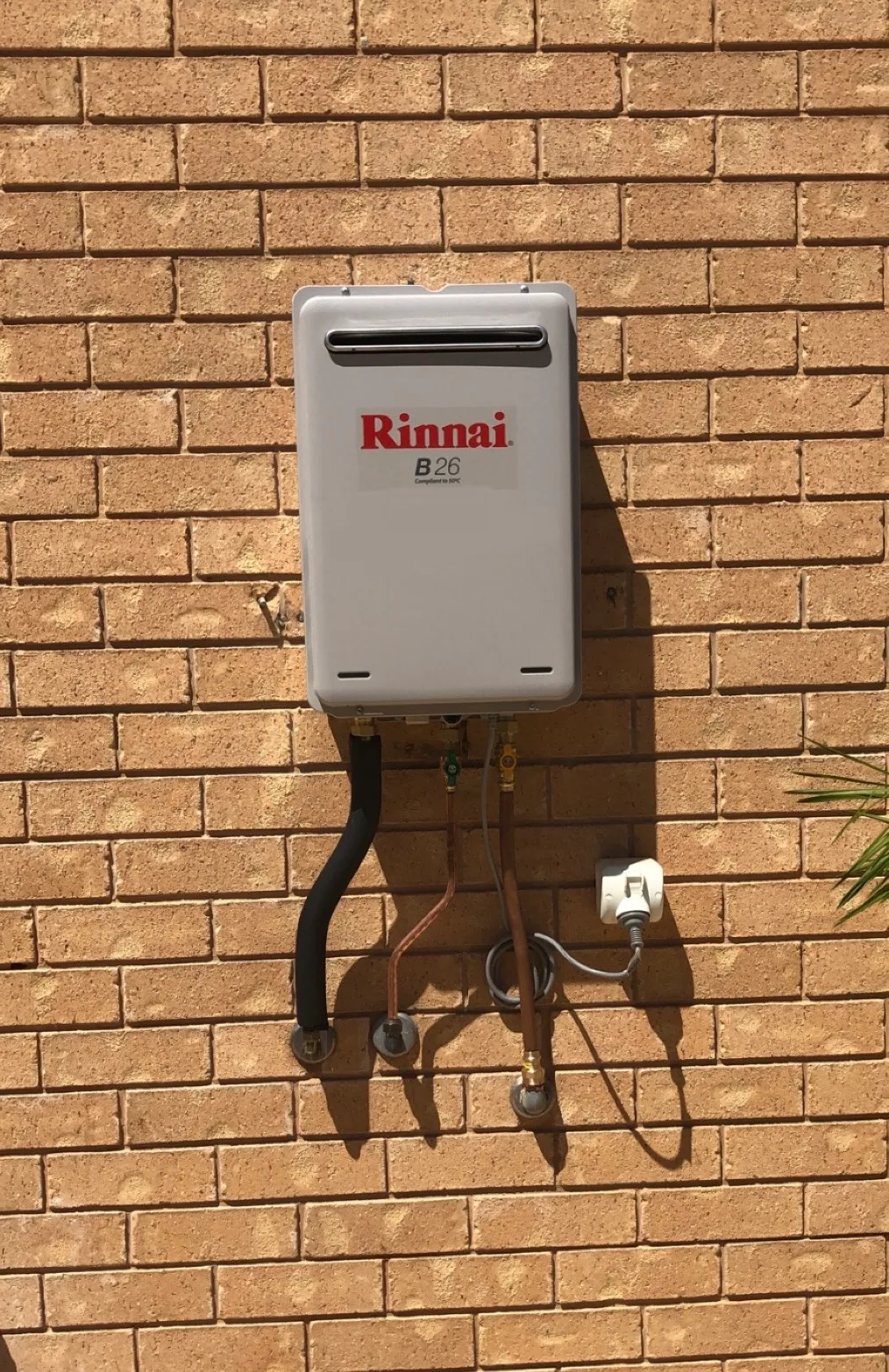 Rinnai continuous flow hot water unit on a cream brick wall