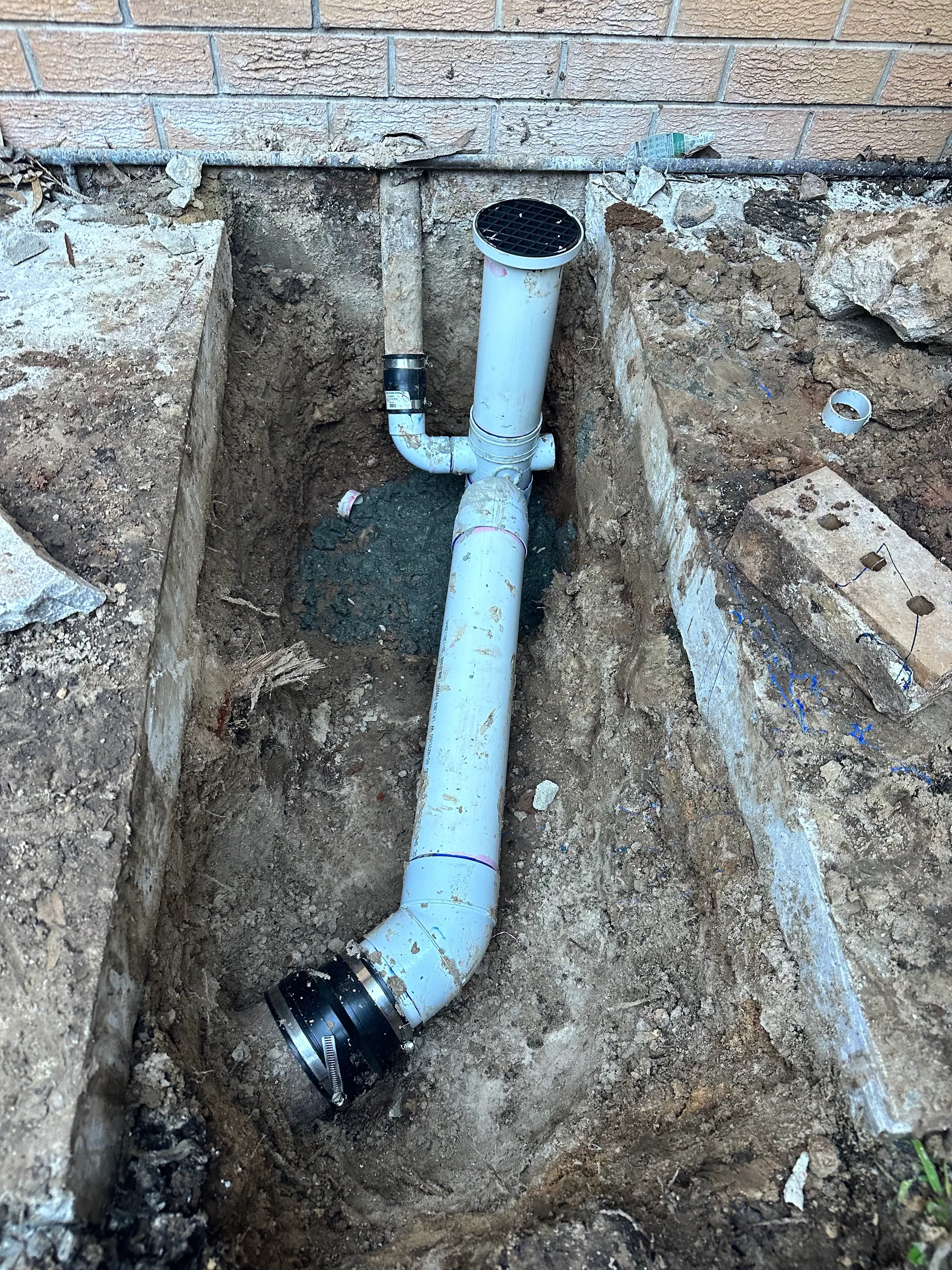 Excavated trench with new PVC drain pipe and a rubber coupling