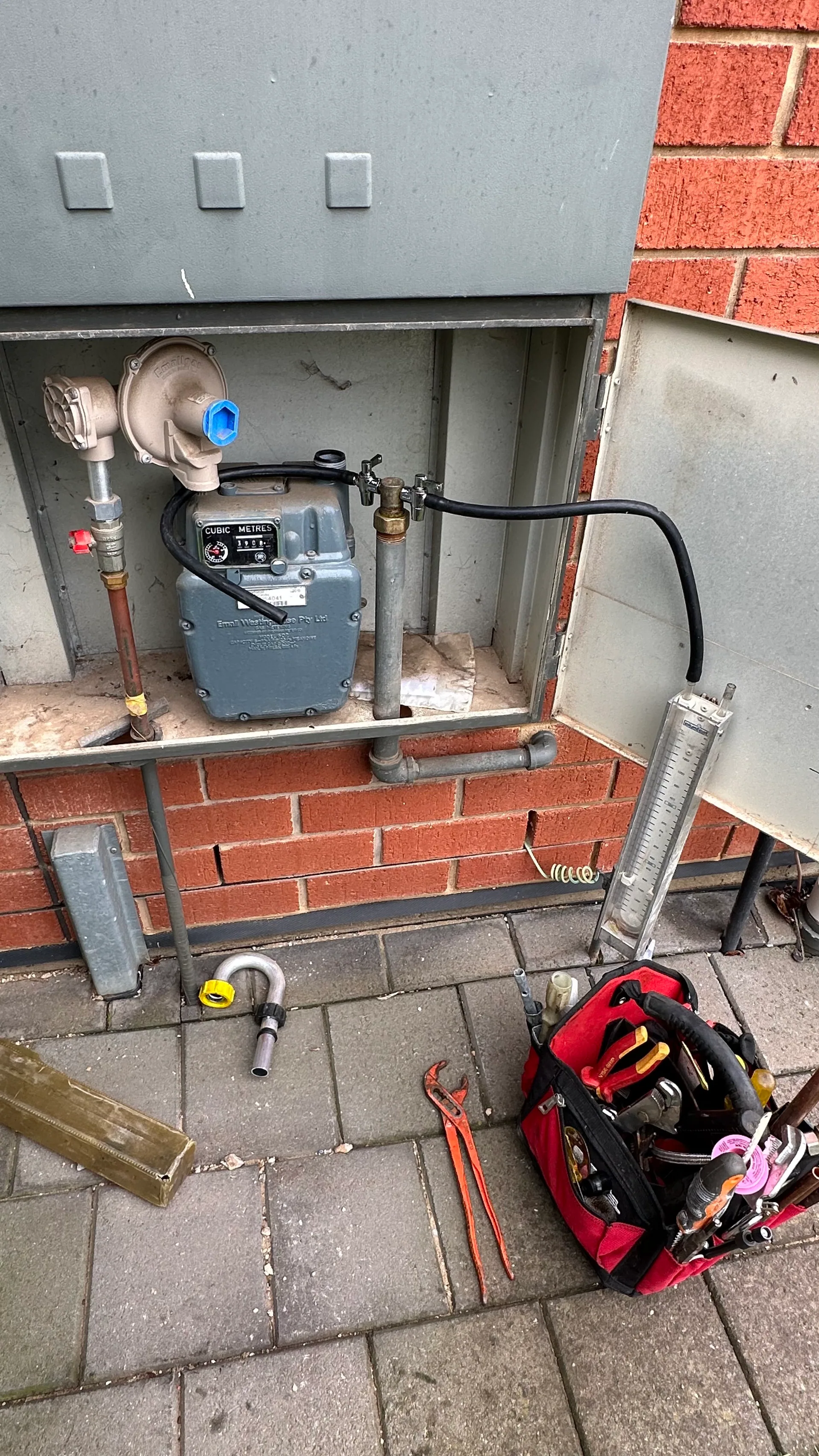 Gas meter with a pressure test gauge set up beside a toolbag