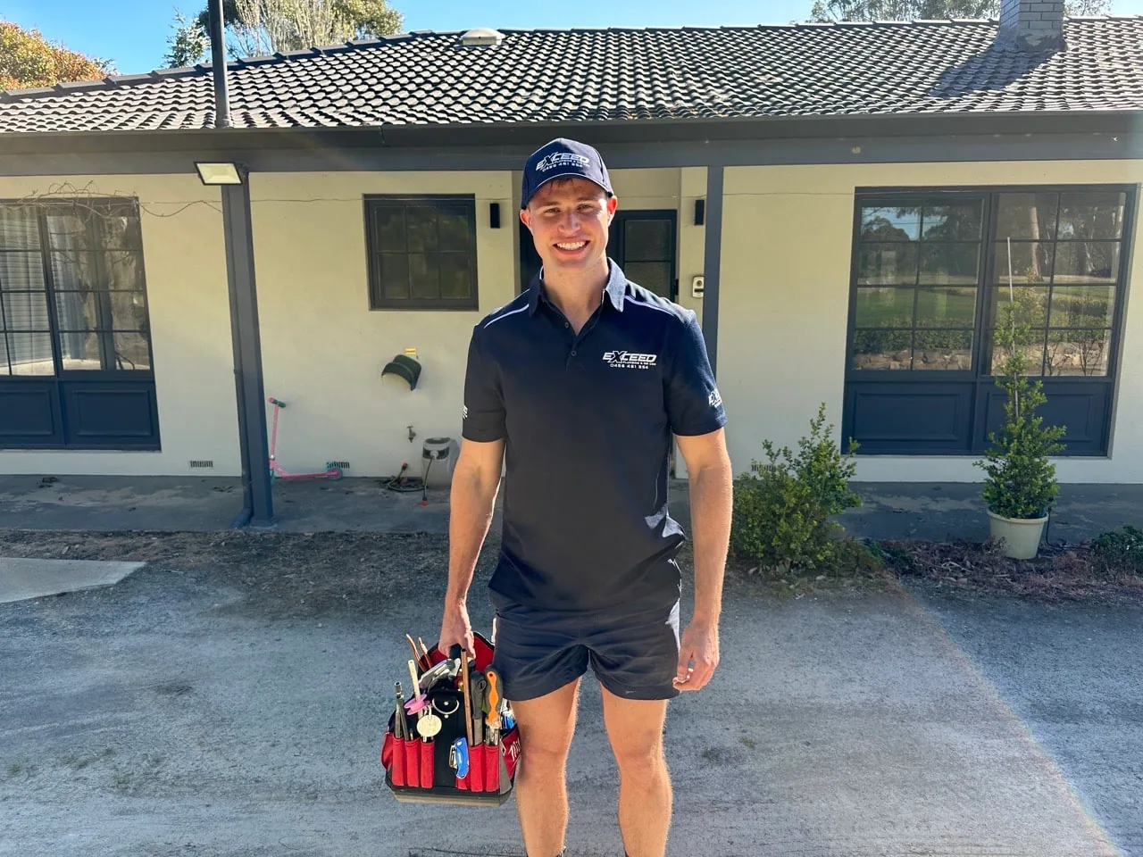 Exceed Plumbing plumber with a toolbag outside a house