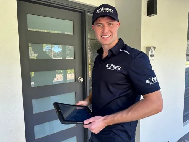 Smiling Exceed Plumbing plumber holding a tablet at a front door