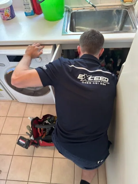 Exceed Plumbing plumber working under a laundry trough