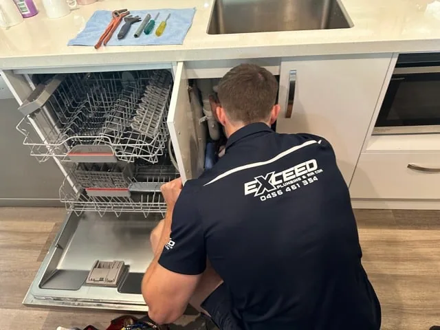 Exceed Plumbing plumber working beside an open dishwasher