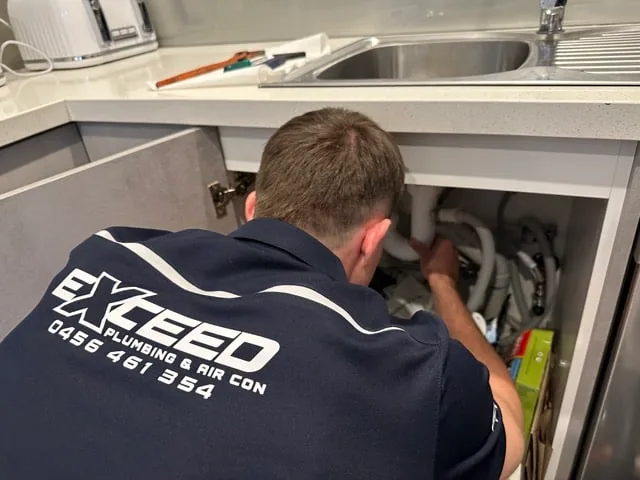 Exceed Plumbing plumber working under a kitchen sink