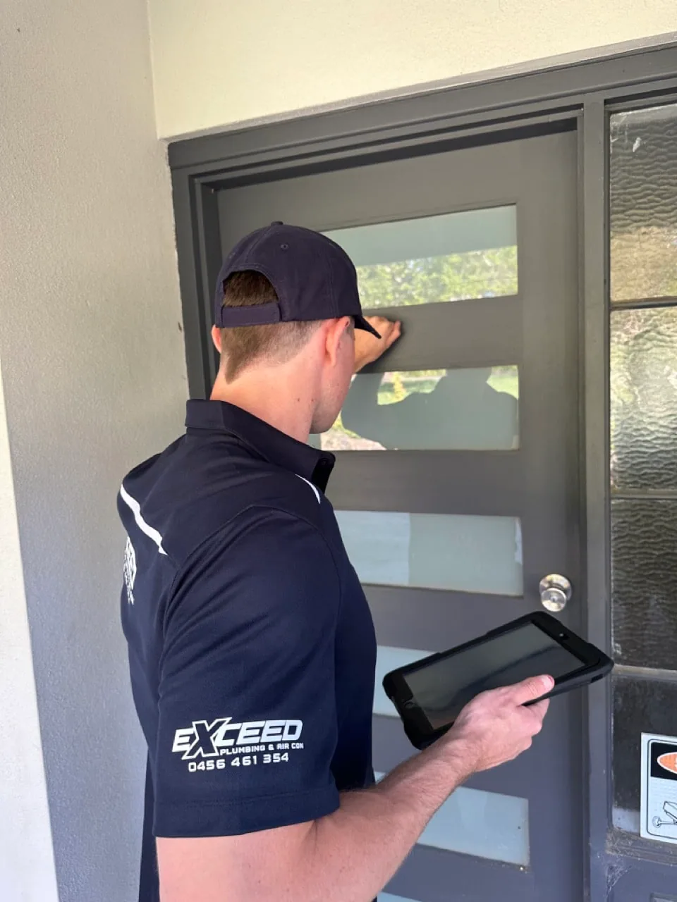 Exceed Plumbing plumber knocking on a front door with a tablet in hand