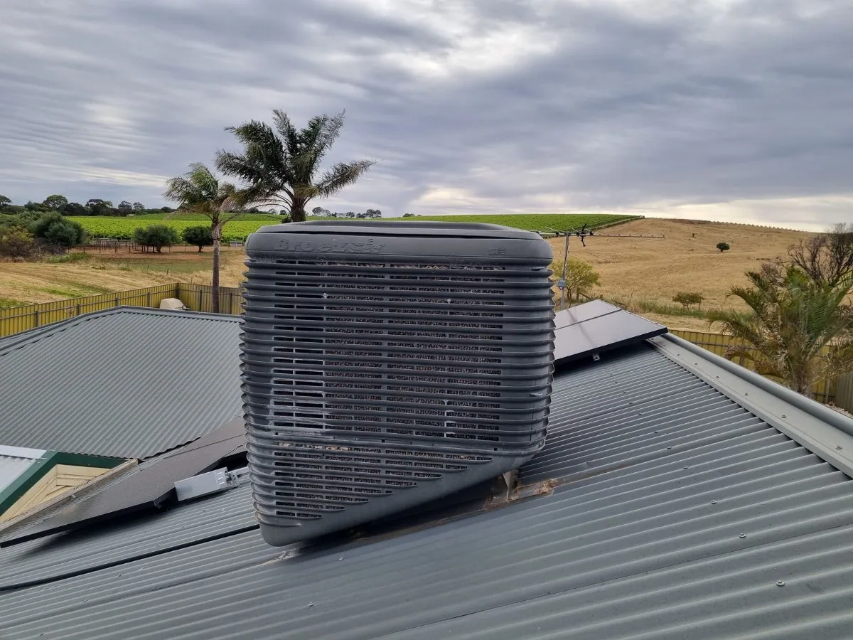 Evaporative cooler on a metal roof beside solar panels